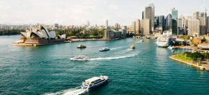 Boats on the water next to Sydney Opera House and tall city buildings