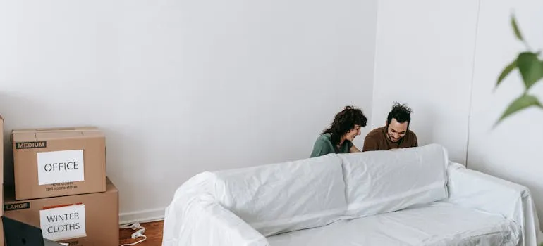 A couple wrapping a couch in a sheet