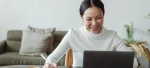 A woman using a laptop and a notebook.