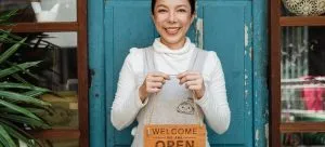 A woman holding a sign we are open after the process of moving a small business in HK.